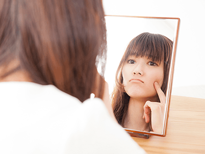 鏡の前でにきびを気にする女性